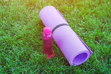 Close up Yoga mat roll with bottle on green grass ready for practice and relax with yoga,Recreation Concept