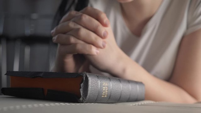 girl praying indoors at bedtime on bible. religion concept evening prayer woman brunette hands on bible praying lifestyle by bed