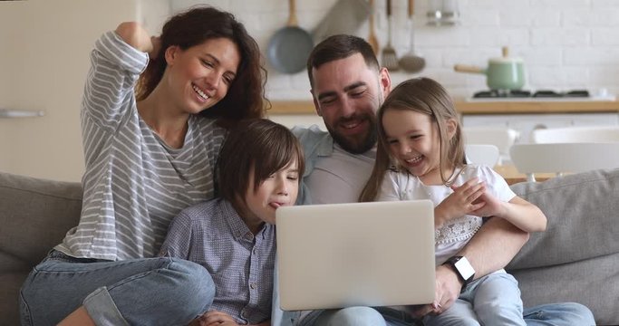Happy family of four parents mum dad and little kids children enjoy using laptop having fun together watching cartoons online make video call internet shopping looking at computer sit on sofa at home