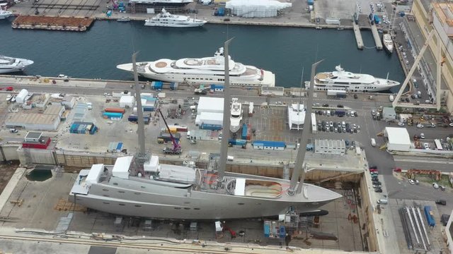 Aerial view of sea dry dock in La Ciotat city, France, the cargo crane, boats on repair, a luxury sail yacht and motor yacht, mountain is on background, shipyard