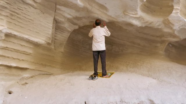 Rear back shot of a muslim man praying to god outdoor in nature in rock formations of a canyon