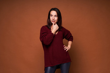 Young happy and positive woman thinking holding her finger on face on brown background