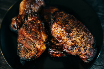 A black plate full of smoked pork chops from an outdoor barbecue grill smoker