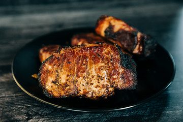 A black plate full of smoked pork chops from an outdoor barbecue grill smoker
