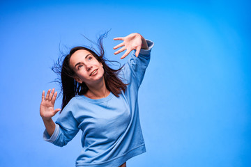 Young happy and positive woman celebrating with raised hands on blue background