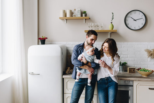 Beautiful caucasian family of three in the kitchen, mother, father and baby girl