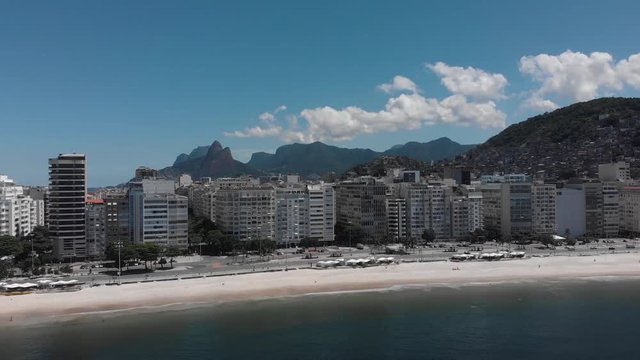 Approach of Copacabana neighbourhood with Two Brothers mountain, Cantagalo shantytown and wider Rio de Janeiro cityscape behind an almost empty beach during the Corona virus outbreak