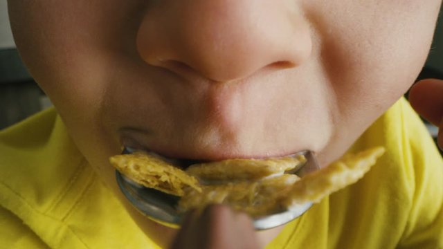 Spoon perspective of boy taking big bite of cereal while eating breakfast