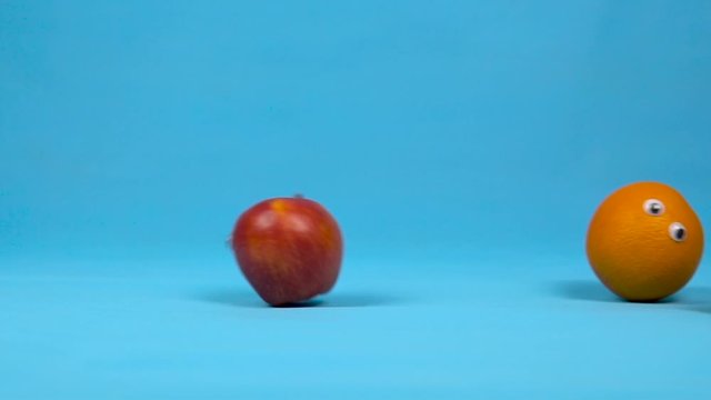 Fruit with eyes roll slowly. Lemon, apple, orange, roll, and then a cucumber falls on a blue background. Slow motion.