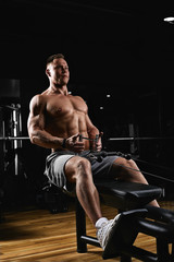 Fototapeta na wymiar Side view of a strong young man with athletic body doing exercises on fitness equipment in a dark gym. Copy space, advertising banner, fitness motivation, healthy body healthy mind