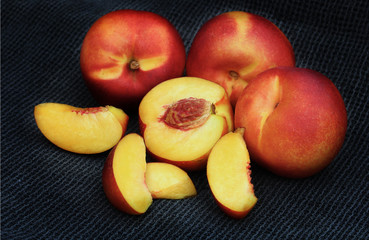 Naklejka na ściany i meble A still life of group of yellow flesh nectarines. One is cut in half and there are also slices of nectarine scattered. Background of black cloth.