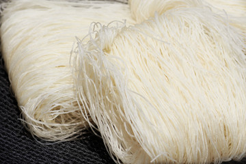 Dry uncooked rice noodles or rice vermicelli on a black cloth background
