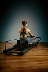 Young girl doing pilates exercises with a reformer bed. Beautiful slim fitness trainer on reformer...