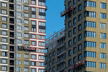 Fototapeta na wymiar Finishing of a high-rise residential building with workers in construction cradles