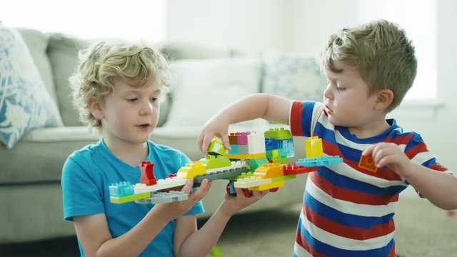 2 boys work together to build a spaceship out of building blocks in slow motion