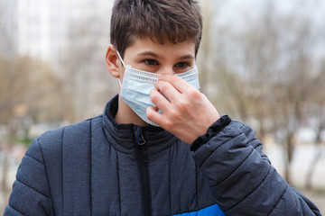 Young cute caucasian boy wearing protective mask against the corona virus on the street. Teenager in surgical  face mask to prevent from virus Covid 19 in the city.  Close up portrait