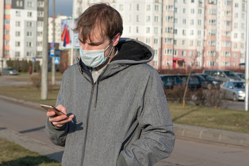 the man on the street with a mobile phone in his hands. face mask to protect against viruses....
