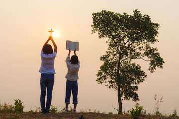 children holding cross and book praying at the sunset. Praise and worship concept: