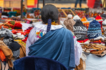Indigenous women in traditional clothing and hairstyle by her market stall on the sunday art and craft market of Otavalo, North of Quito, Ecuador. - obrazy, fototapety, plakaty