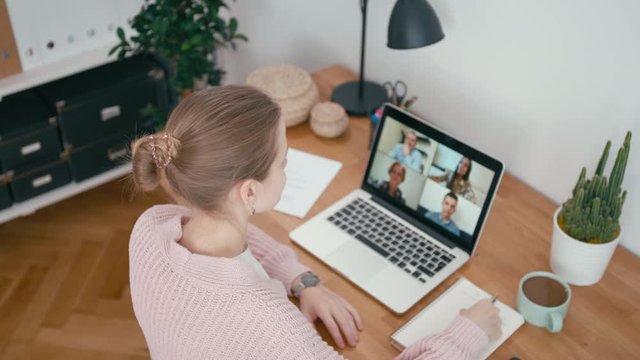 Online Group Video Call Conference of Work Team from Home Office. Woman Greets and Talks with 4 People at Video Chat using Laptop. Self-isolation at COVID-19 Pandemic. 4K Top View Orbit Shot