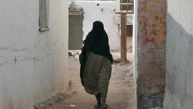 Muslim woman walking in an alley covering her face with her hijab