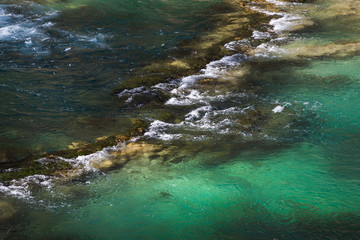 Stones under the surface of a small waterfall with clear turquoise water in Huancaya town, Lima Region, Peru