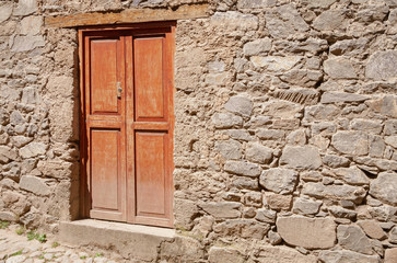 Wooden door at the entrance of a traditional clay house at a sunny day on a street of Huancaya, Lima Region, Peru