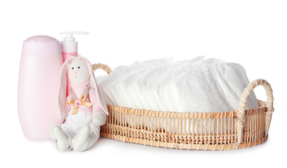 Fototapeta na wymiar Wicker tray with disposable diapers, toy bunny and toiletries on white background
