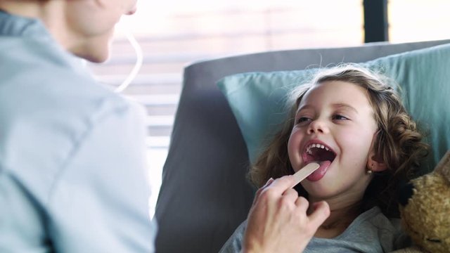 Female doctor examining small girl in bed in hospital.