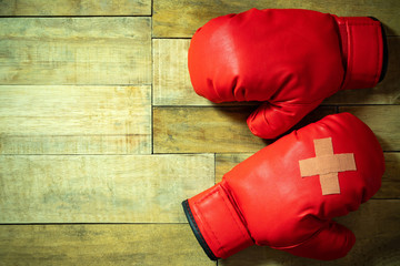 Red boxing gloves placed on wooden floor at the gym. Adhesive plaster across each other on boxing gloves. Idea of getting hurt or combat losing business rivals. Concept of fighting giving up boxing.