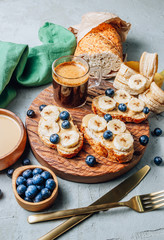 Buckwheat healthy bread with peanut butter, banana and blueberry on wooden board over concrete background. Selective focus. Summer breakfast.