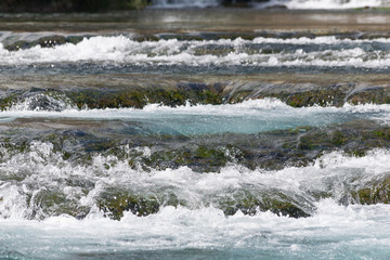 Stones under the surface of a small waterfall with clear turquoise water in Huancaya town, Lima Region, Peru