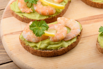Sandwiches with avocado cream and shrimp on a cutting board.
