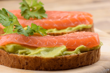 Sandwiches with avocado cream and slices of salmon on a cutting board.