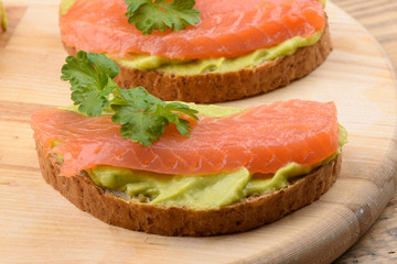 Sandwiches with avocado cream and slices of salmon on a cutting board.