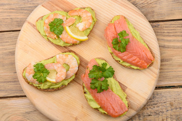 Sandwiches with slices of salmon and shrimp decorated with parsley and lemon.
