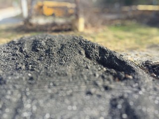 Naklejka premium Pile of Hot Asphalt Petroleum Pile Black Resin Raw Bitumen at a road under road construction. Yellow School bus in the background.
