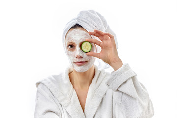 Beautiful young woman with white cream face and juicy fresh cucumbers on her eyes. White isolated background.