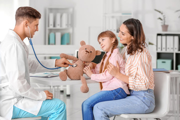 Pediatrician with toy showing little girl how to use stethoscope in clinic