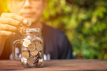 Close up of A man's hand is putting a coin in a glass jar, Concept of saving money