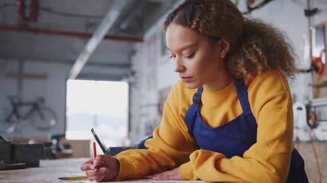 Female business owner in workshop making notes on plan for bicycle - shot in slow motion