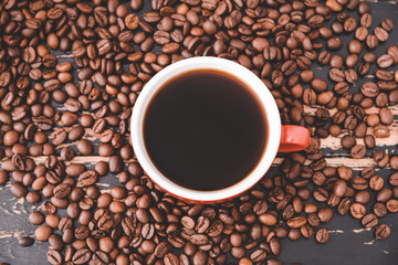 Cup of hot coffee and beans on wooden background