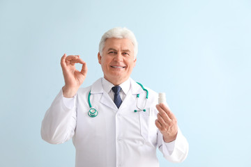 Senior doctor with pills on color background