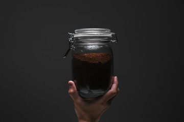 One hand holding a jar of blended coffee bean with spotlight effect and isolated dark grey background