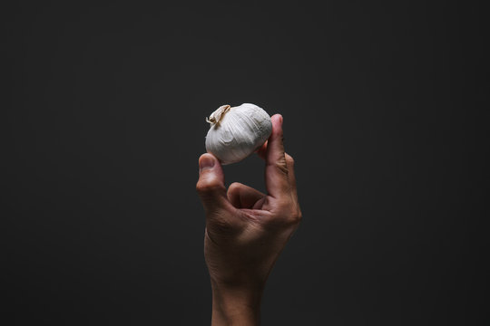 One hand holding a piece of whole garlic with spotlight effect and isolated dark grey background