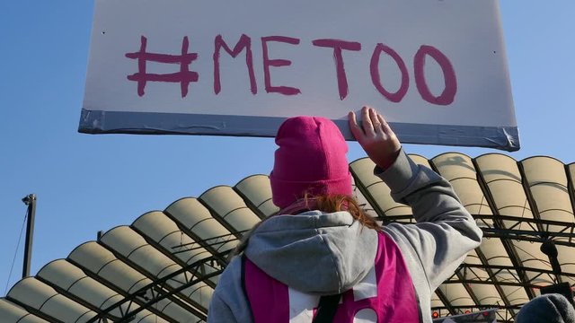Low angle rear back shot of a girl holding a #MeToo sign with blue sky in background