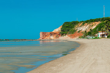 Sunny morning, where you can see boats, houses and the cliff with vegetation in the background in Praia Redonda, Icapui, Ceara, Brazil on April 23, 2016