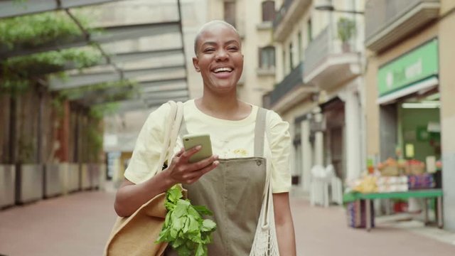 Slow motion shot of woman with grocery bag using smartphone in city