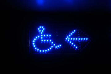 Illuminated blue led signage indication / pointing to were the disability access is. Arrow and person in wheel chair icons.