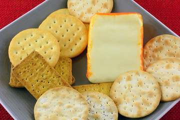 Close up of wedge of Port Salut semi-soft cheese on plate with assorted crackers